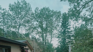 A hot tub with a person relaxing, a patio area with outdoor furniture, and a view of trees and a building in the background.