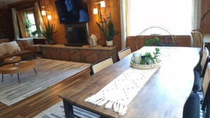 A cozy living room with a TV, wooden walls, a fireplace, and a dining area with a table and chairs.