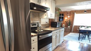 A modern kitchen with stainless steel appliances, wooden cabinets, and a dining area with a table and chairs.