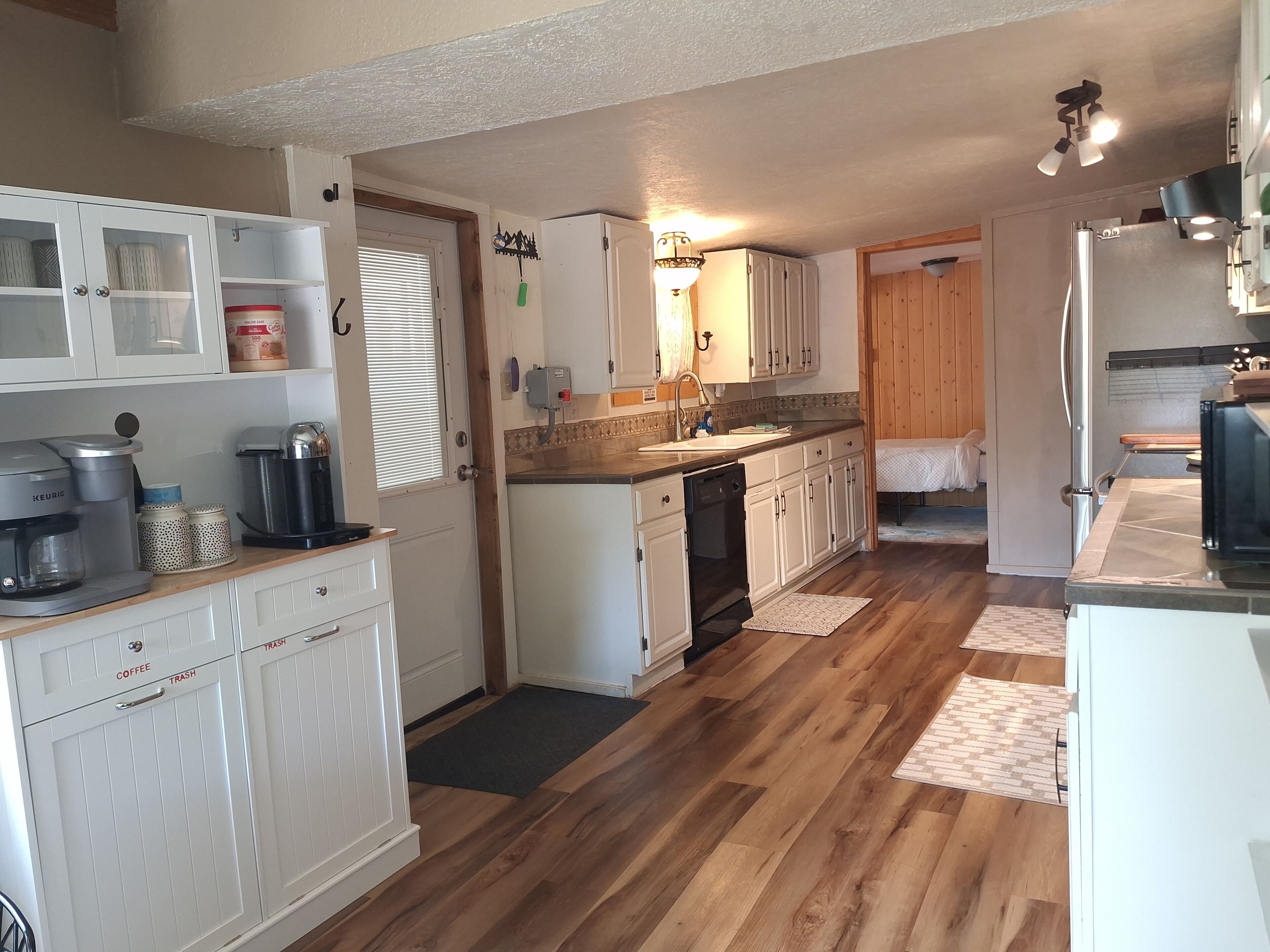 A kitchen with white cabinets, a coffee maker, a dishwasher, and wooden flooring.