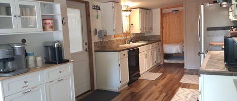 A kitchen with white cabinets, a coffee maker, a dishwasher, and wooden flooring.
