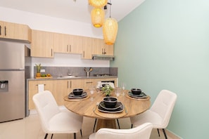 Une cuisine moderne avec des meubles en bois, un réfrigérateur en acier inoxydable, une table à manger agrémentée de bols et d’assiettes noirs, et un luminaire suspendu.