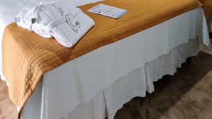 Una cama bien hecha con sábanas blancas y un edredón marrón, dos almohadas y una toalla doblada sobre la cama.