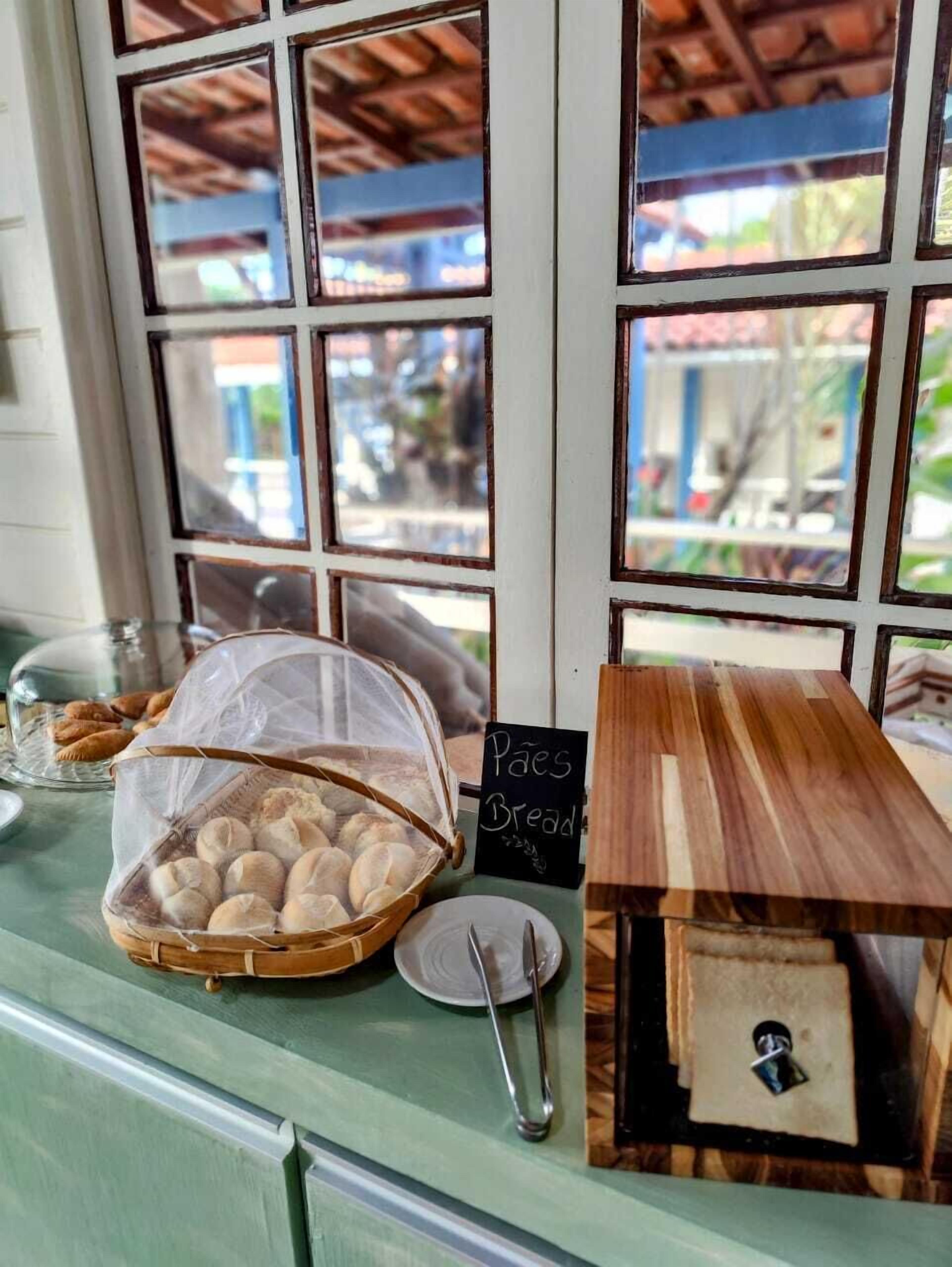 Een bakkerijbalie met een mand brood, een bordje met de tekst 'Pães Bread' en een houten kist met slot.