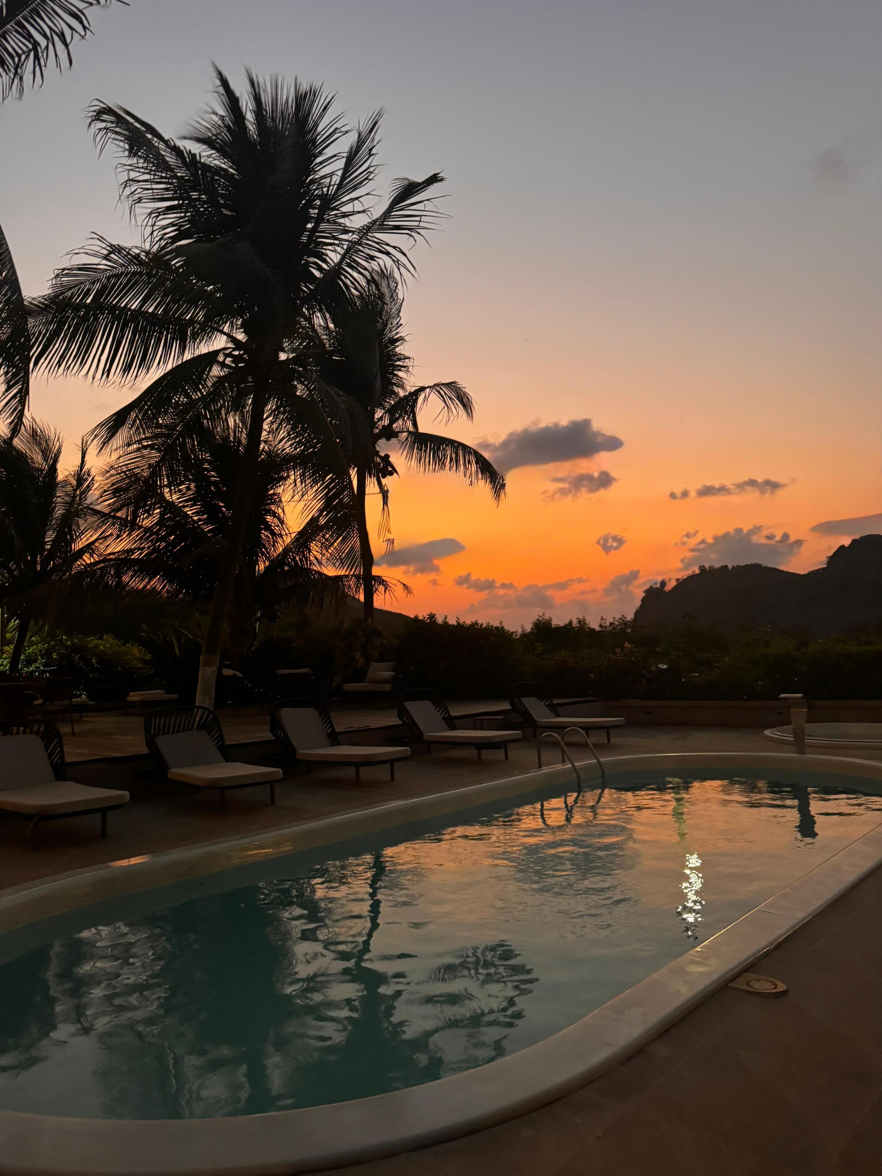 A poolside area with lounge chairs and a pool reflecting the sunset.