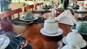Un comedor con una mesa de madera lista para una comida, un cuadro en la pared y vistas al exterior.