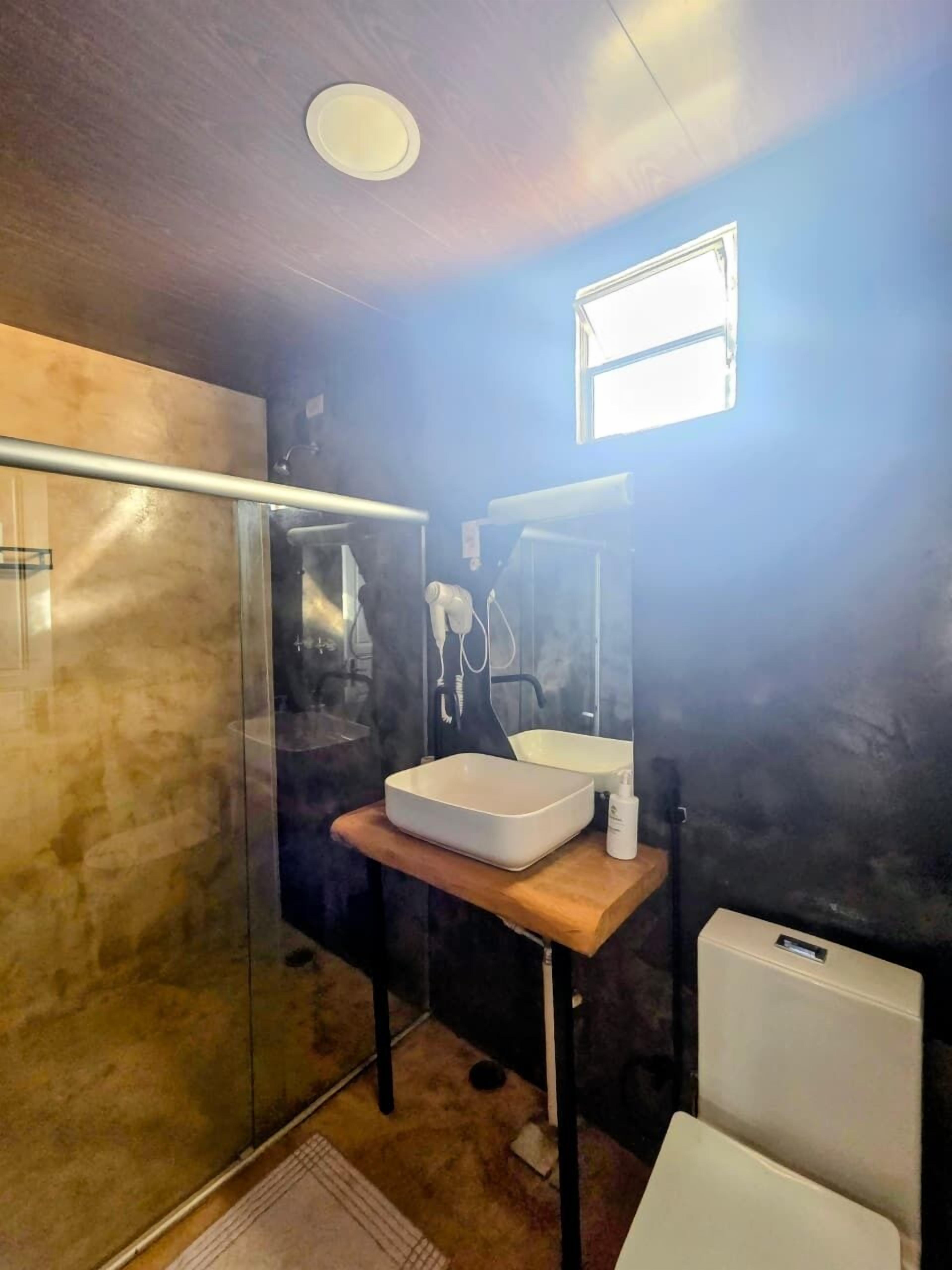A modern bathroom with a glass shower enclosure, a white sink, and a small window.