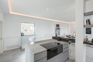 A modern kitchen with a central island, built-in appliances, and a stone accent wall. - Villa De Boer, brand new amazing seafront in Amalfi coast, private pool and garden (Piano di Sorrento)