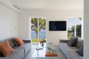 Ein modernes Wohnzimmer mit zwei grauen Sofas, einem Glastisch und einem an der Wand montierten Flachbildfernseher.