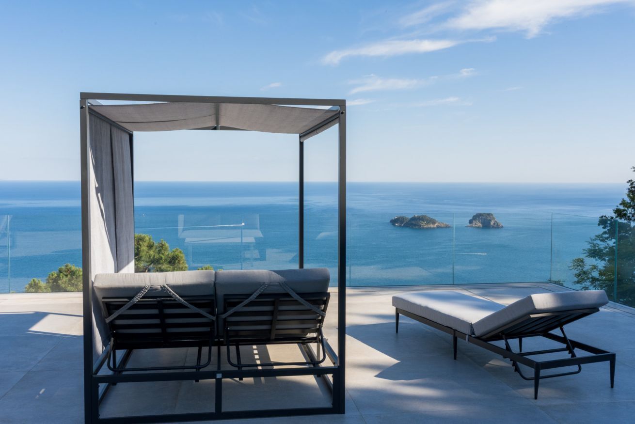 A balcony with a view of the sea, a sun lounger, and a covered seating area.