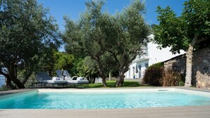 Una piscina con lettini, circondata da alberi e un edificio bianco.