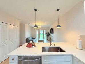 A modern kitchen with a central island, pendant lighting, and a view into a living area. - Stylish Comfort in Englewood – 3/2, Great Location (Englewood)