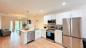 A modern kitchen with white cabinets, stainless steel appliances, and a wooden floor. - Stylish Comfort in Englewood 3BR 2BA, Great Location (Englewood)