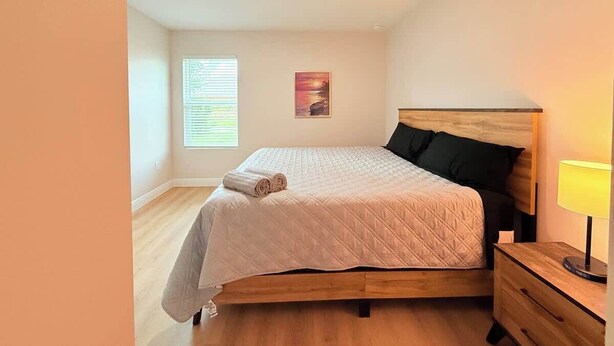 A bedroom with a bed, a nightstand, a lamp, a window with blinds, and a wall-mounted picture. - Stylish Comfort in Englewood 3BR 2BA, Great Location (Englewood)