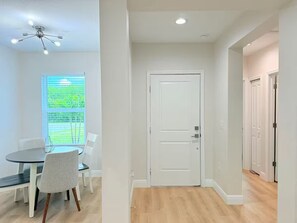 A room with a dining table, chairs, a ceiling fan, a white door, and a view of greenery outside. - Stylish Comfort in Englewood – 3/2, Great Location (Englewood)