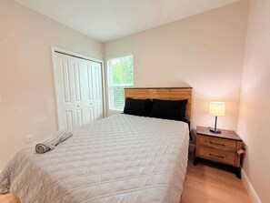 Une chambre à coucher avec un lit, une table de chevet avec une lampe, une porte et une fenêtre.