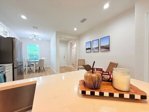 A modern kitchen with a refrigerator, dining table, chairs, and a wooden cutting board with a decorative bowl and a glass jar. - Stylish Comfort in Englewood – 3/2, Great Location (Englewood)