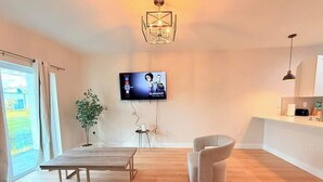 A modern living room with a wooden floor, a dining table, a sofa, a TV mounted on the wall, and a pendant light. - Stylish Comfort in Englewood 3BR 2BA, Great Location (Englewood)
