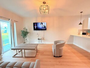 A modern living room with a wooden floor, a dining table, a sofa, a TV mounted on the wall, and a pendant light. - Stylish Comfort in Englewood 3BR 2BA, Great Location (Englewood)