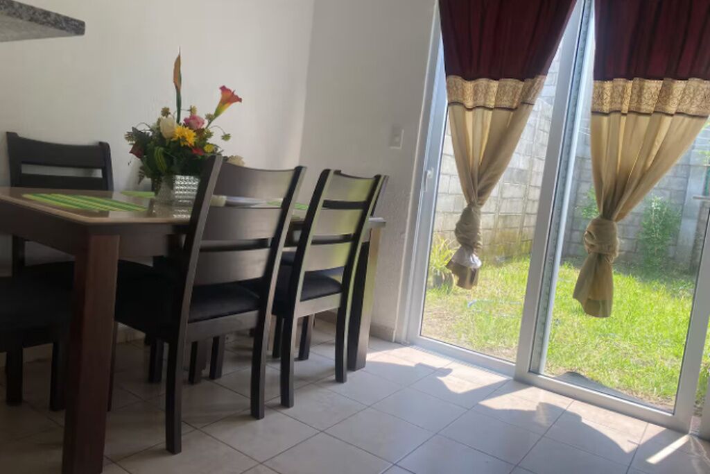 A dining area with a table and chairs, a vase with flowers, and a view through a glass door to a garden.