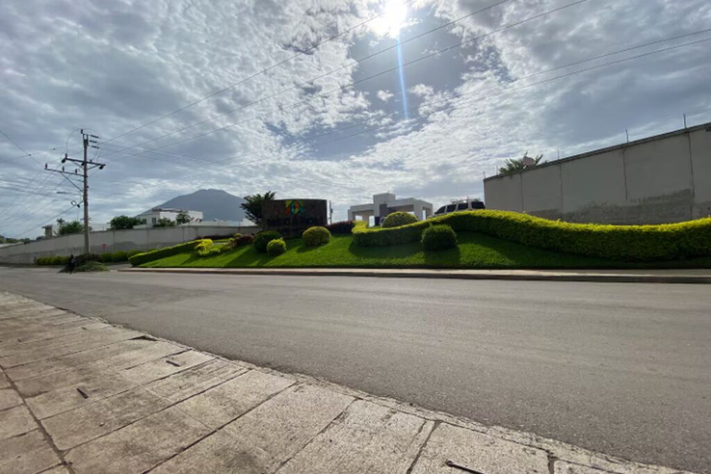 A road with a sidewalk, a building with a sign, and a mountain in the background.