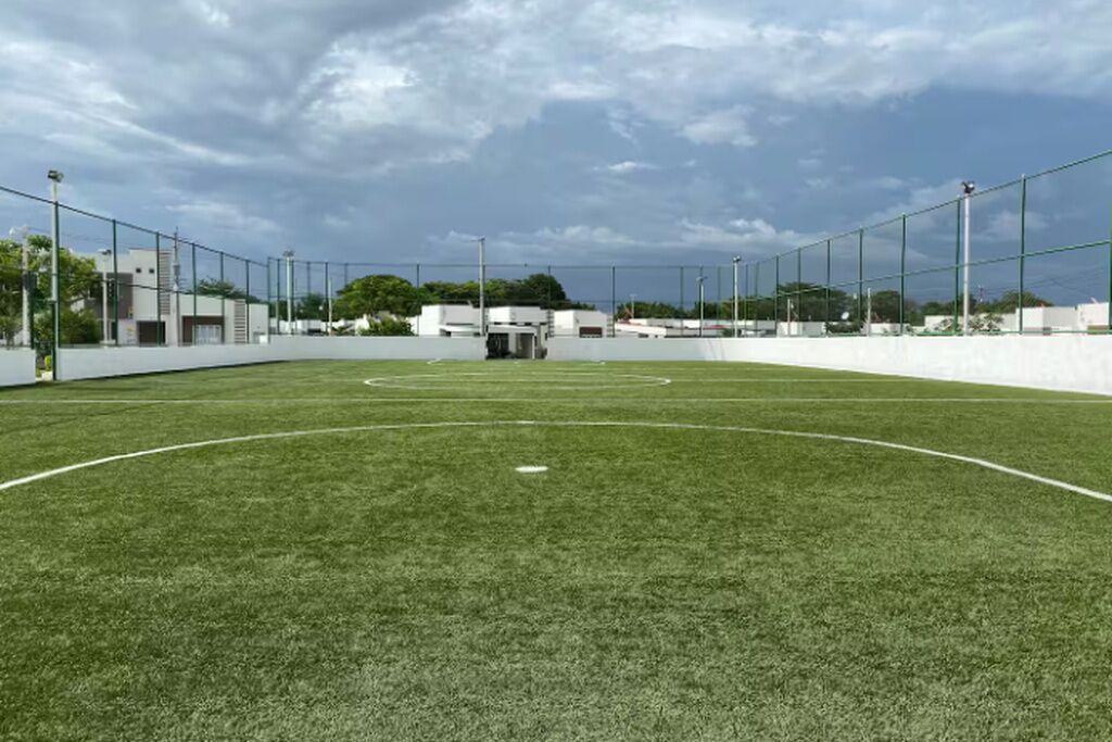 Un campo de fútbol con porterías, focos y un edificio al fondo.