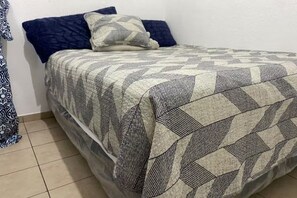 A bed with a patterned bedspread, a pillow, and a blue pillow on a tiled floor. - Spacious 7-bedroom house in beautiful San Miguel with AC (San Miguel)