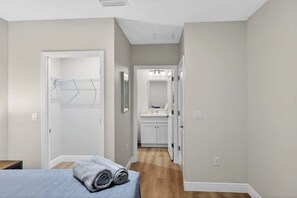 Un dormitorio con cama, vestidor y baño con lavamanos y espejo.