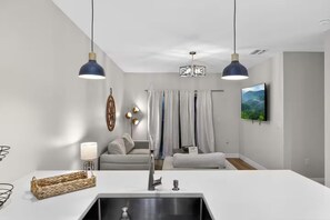 Een moderne keuken met een wit aanrecht, een roestvrijstalen spoelbak en hangende lampen.