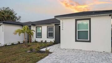 A row of modern single-story buildings with numbered windows, a paved driveway, and a small palm tree.