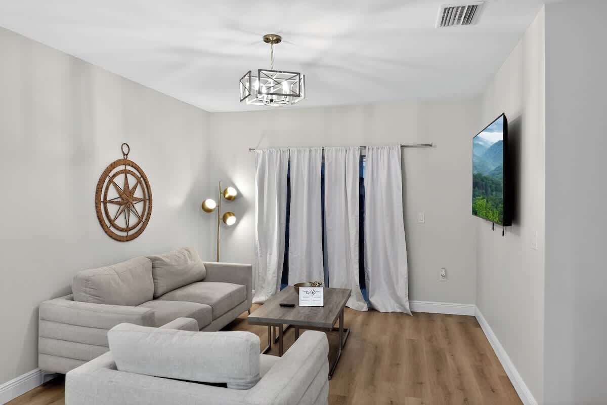 A modern living room with a sofa, a coffee table, a wall-mounted TV, and a decorative wheel on the wall.
