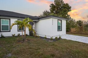 A modern house with a white exterior, green shutters, and a small palm tree in the front yard. - Relax in Englewood – 3BR/2BA Home Close to Beaches (Englewood)