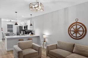 A modern kitchen with white cabinets, a central island, pendant lights, and a decorative compass wall piece. - Relax in Englewood – 3BR/2BA Home Close to Beaches (Englewood)