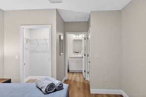 Een slaapkamer met een bed, een badkamer met een wastafel en spiegel, en een gang die naar een keuken leidt.