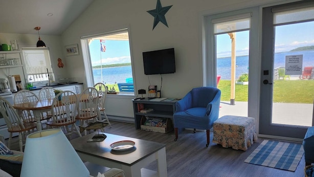 A living room with a dining area, a television, and a view of the sea. - Tiny Beach House (Cocagne)