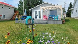A residential property with a deck, outdoor seating, and a garden with various flowers. - Tiny Beach House (Cocagne)