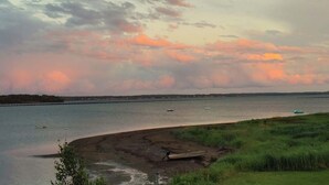A coastal landscape with a body of water, boats, and a grassy area with a small structure. - Tiny Beach House (Cocagne)