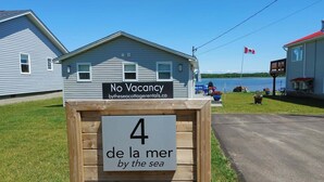 A small cabin with a sign indicating no vacancy and a sign below stating '4 de la mer by the sea'. - Tiny Beach House (Cocagne)