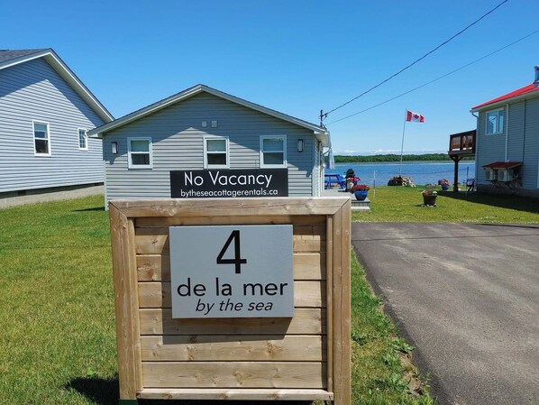 A small cabin with a sign indicating no vacancy and a sign below stating '4 de la mer by the sea'.