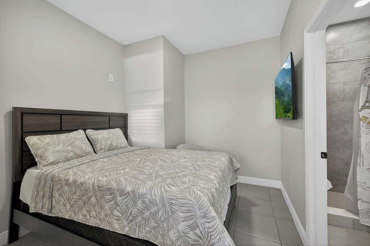 A bedroom with a bed, a mounted TV, and a shower area with a tiled wall.