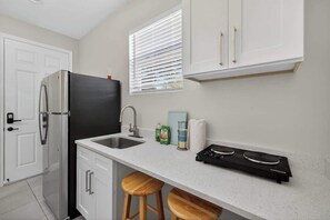 Una cocina funcional con refrigerador, lavamanos, estufa y taburetes de madera.