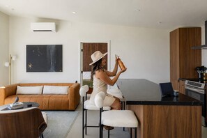 Eine moderne Küche mit einer zentralen Kochinsel, einem Essbereich mit einem braunen Sofa und einer Person, die auf einem Barhocker sitzt.