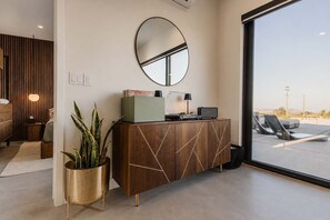 Ein modernes Interieur mit einem Holzschrank, einem runden Spiegel und Blick durch ein großes Fenster.