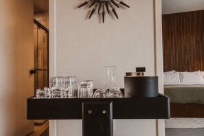 A hotel room with a bed, a bedside table with glasses and a container, and a wall-mounted decor piece. - Desert Haus · Pool, Hot Tub, Fire Pit, Views (Joshua Tree)