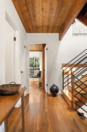 A wooden staircase with a metal railing, a wooden table with a vase, and a view into a room with a chair and a window. - Spacious 3BR/ 2BA Topanga Home – Nature Retreat w AC and Laundry (Topanga)