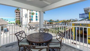 Uma varanda com mesa e cadeiras, com vista para uma praia e um edifício com uma placa que diz 'Nervous Nellie's Happy Spring Break'.