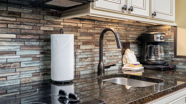 Cozinha com painel de backsplash de pedra, eletrodomésticos de aço inoxidável e armários brancos.