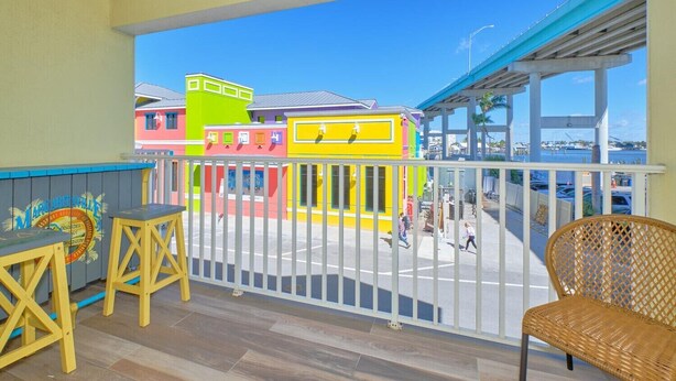 A balcony with a view of colorful buildings, a street, and a body of water. - Harbour House #212 "Shore Thing" (Fort Myers Beach)