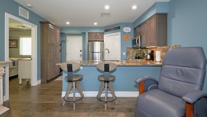 A modern kitchen with a bar area, wooden cabinets, and a gray leather chair. - Harbour House #212 "Shore Thing" (Fort Myers Beach)