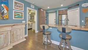 A kitchen with a central island, bar stools, a refrigerator, and a dining area. - Harbour House #212 "Shore Thing" (Fort Myers Beach)